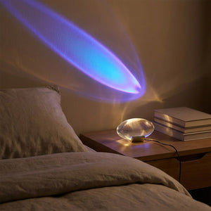 Lampe cristal projetant un halo bleu violet sur une table de chevet à côté d'un lit fait