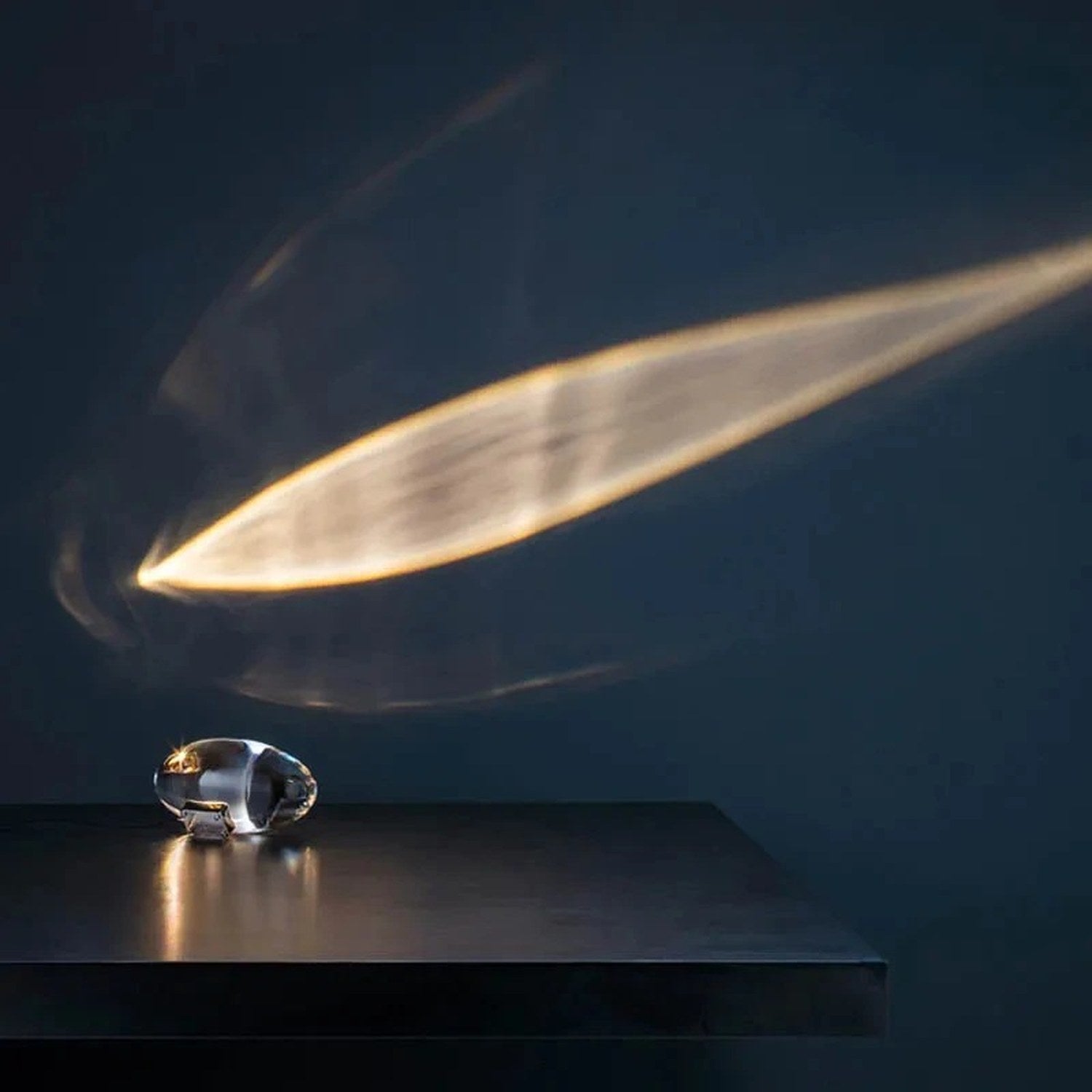Lampe cristal ovale posée sur une table sombre projetant un halo doré incliné sur le mur