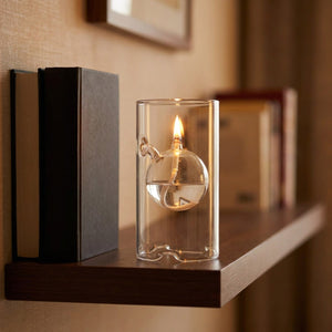 Lampe à huile ouragan transparente posée sur une étagère près de livres