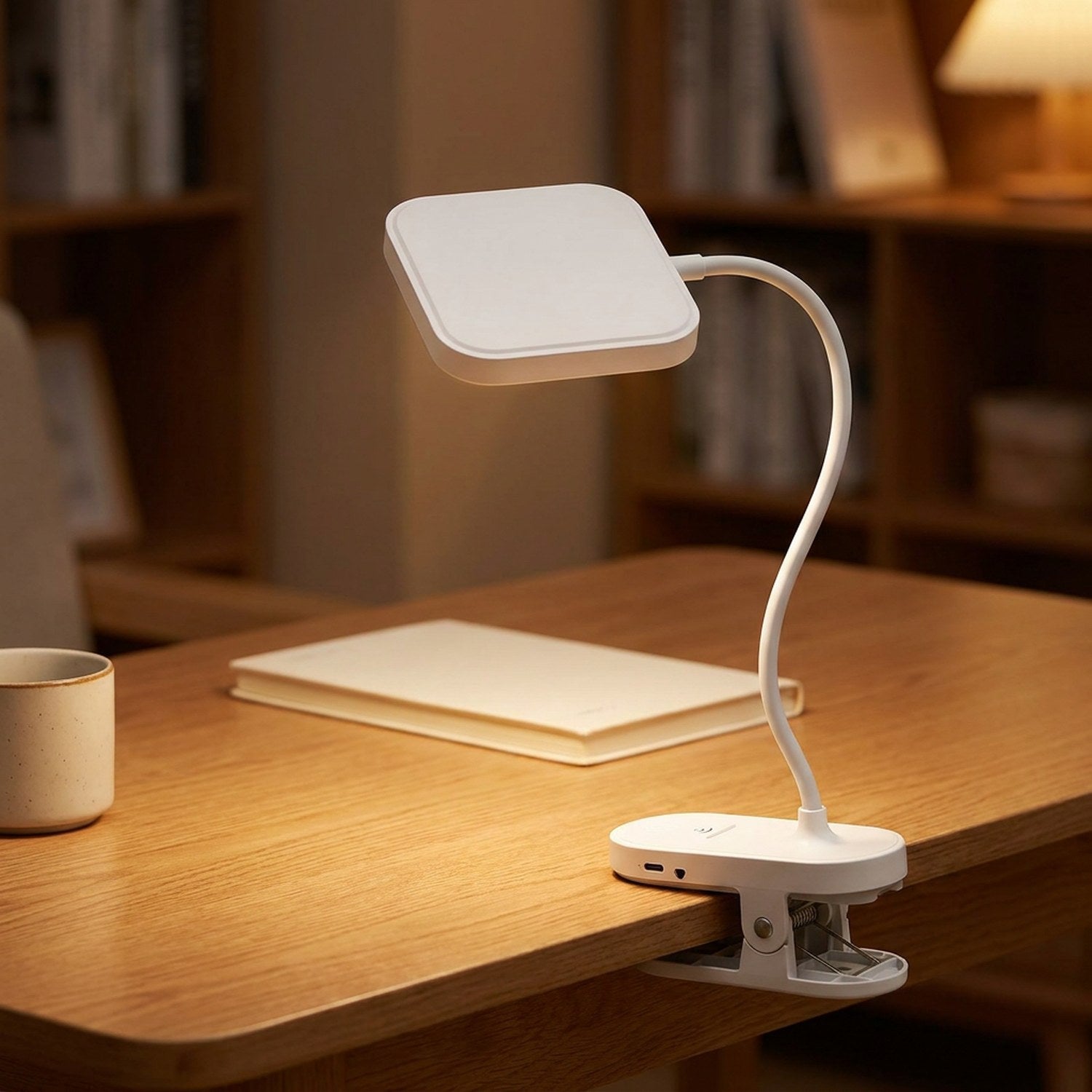 Lampe de bureau à pince LED blanche avec col de cygne flexible posée sur un bureau en bois