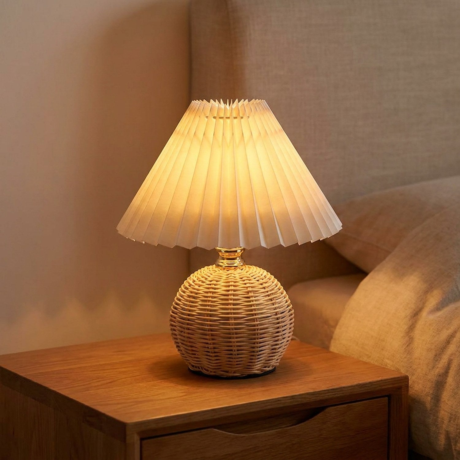 Lampe de chevet à base en rotin tressé et abat-jour plissé blanc allumée sur une table de nuit