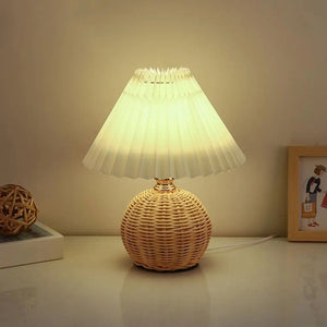 Lampe de chevet en rotin et abat-jour plissé allumée posée sur un meuble clair