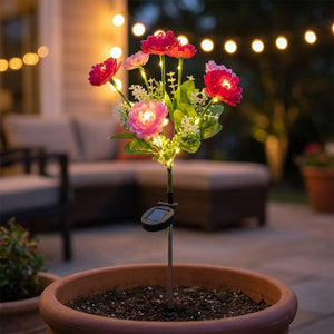 Lampe solaire a fleurs plantee dans un pot de terrasse le soir