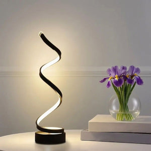 Lampe design spirale LED allumée à côté d'un vase de fleurs violettes