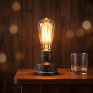 Lampe tuyau industrielle allumée sur un comptoir de bar en bois avec un verre