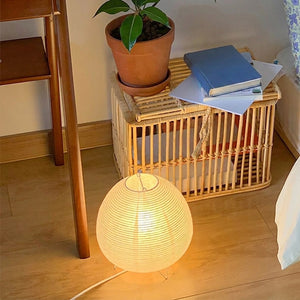 Lampe wabi-sabi en papier de riz allumée au sol près d'une chaise en bois et d'une plante verte