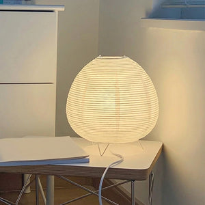 Lampe de chevet en papier de riz allumée sur une table près d'un lit avec coussin fleuri