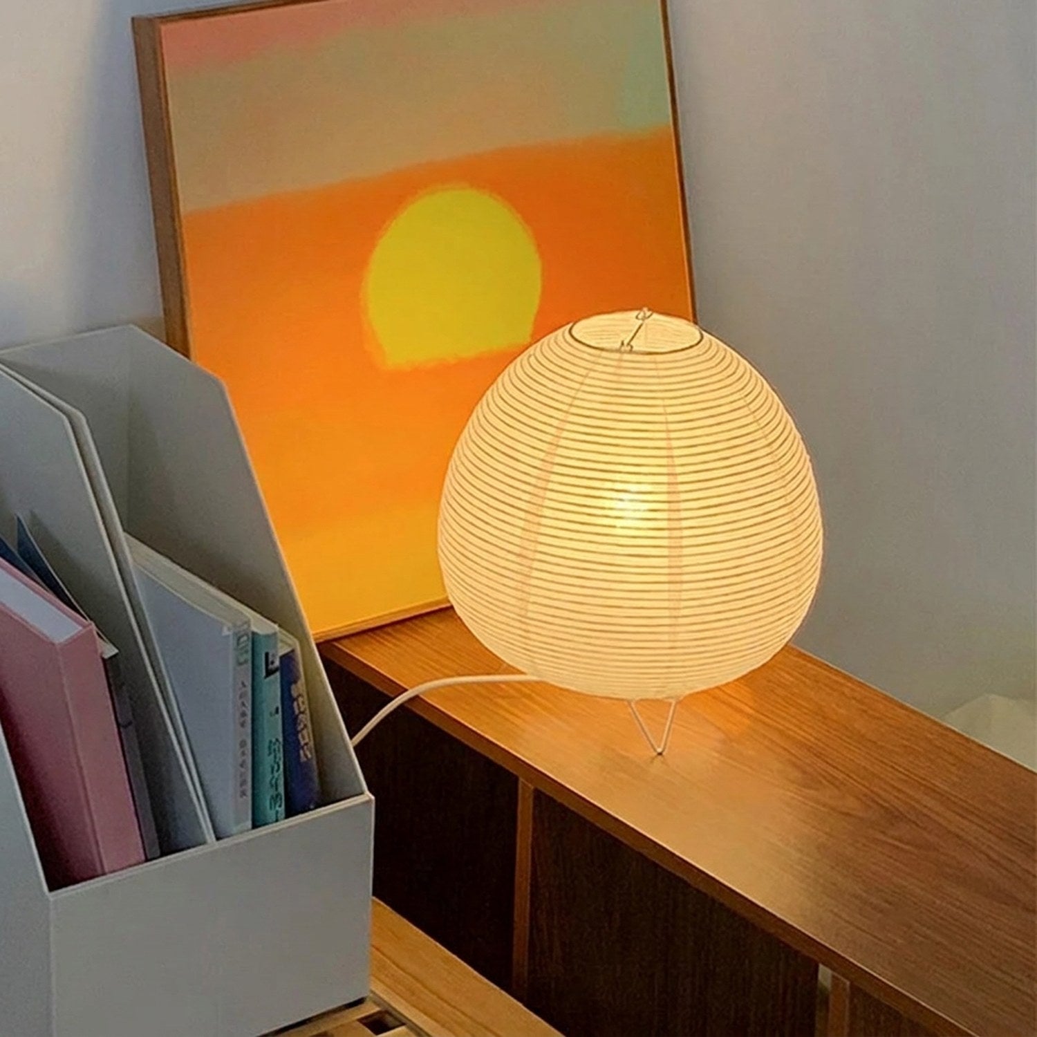 Lampe design allumée sur un meuble en bois avec un tableau coucher de soleil en arrière-plan