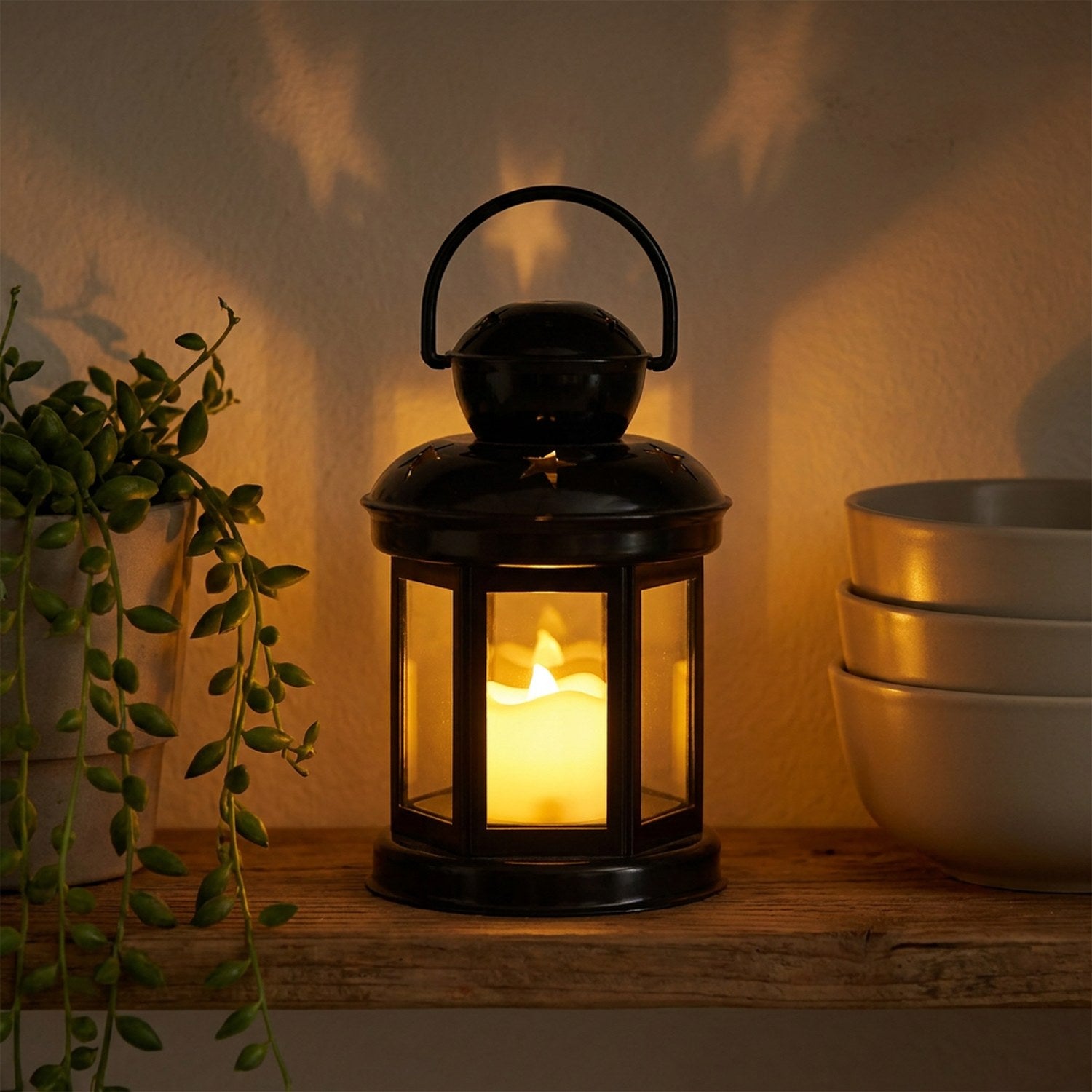 Lanterne étoile noire allumée sur une étagère bohème avec une plante