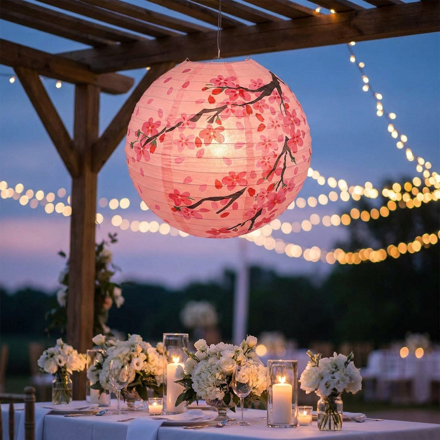 Lanterne japonaise rose ornée de fleurs de pêcher suspendue lors d'une réception de mariage en plein air