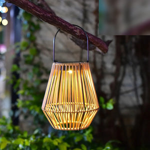 Lanterne géométrique style rotin suspendue à une branche dans un jardin illuminée la nuit