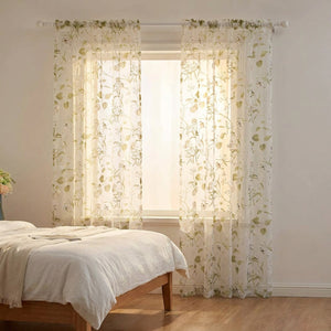 Voilage fleuri vert clair suspendu à la fenêtre d'une chambre cocooning près d'un lit en lin blanc