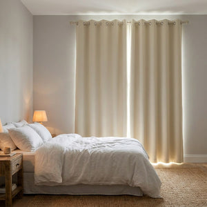 Rideau occultant beige fermé devant une fenêtre dans une chambre chaleureuse