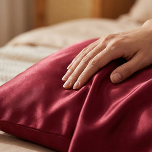 Gros plan sur une main caressant le satin grenat de la taie d'oreiller
