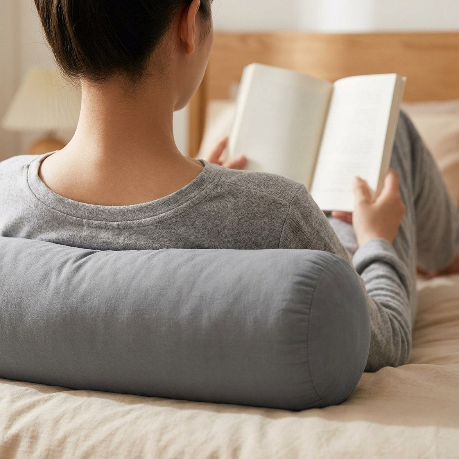 Personne assise dans son lit lisant un livre appuyée contre un traversin gris