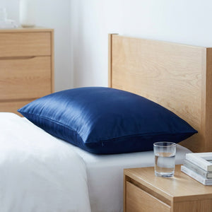 Taie d'oreiller en soie bleu marine sur un lit avec table de chevet en bois clair et livres