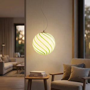 Suspension boule en verre verte en spirale allumée dans un coin lecture cosy avec fauteuil