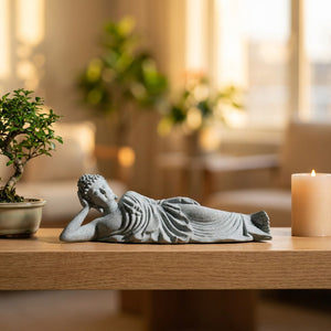 Statue de Bouddha couché en grès posée sur une étagère en bois près d'un bonsaï et d'une bougie