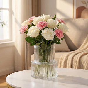 Vase en verre rayé avec roses blanches et œillets roses sur table ronde en marbre dans un salon lumineux