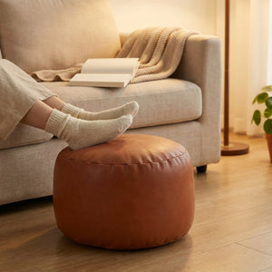 Pouf repose-pieds en simili cuir cognac avec des pieds posés dessus devant un canapé