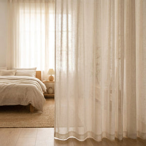 Voilage aspect lin écru habillant une grande fenêtre dans une chambre sereine au style japandi