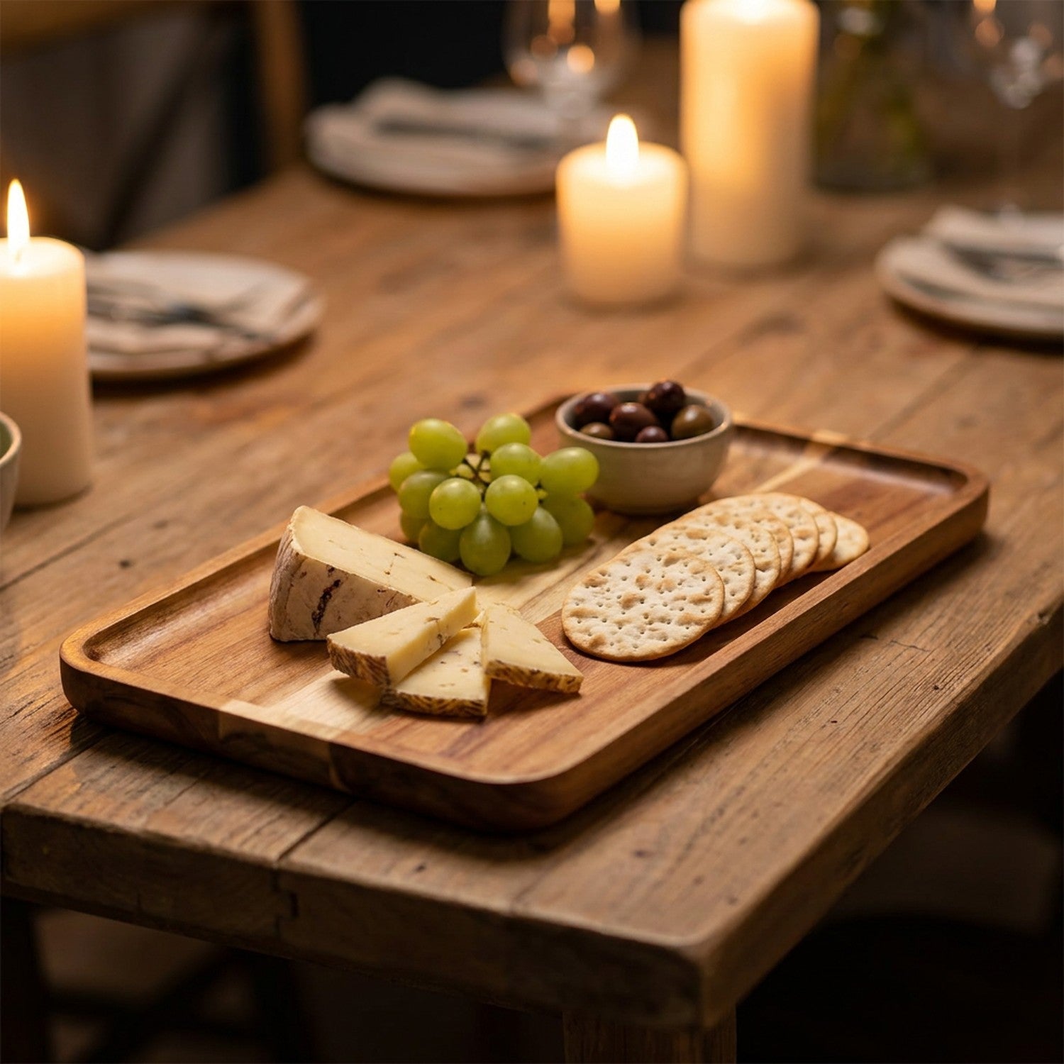 Plateau apéritif en bois d'acacia garni de fromage de raisin et de crackers à la lueur des bougies