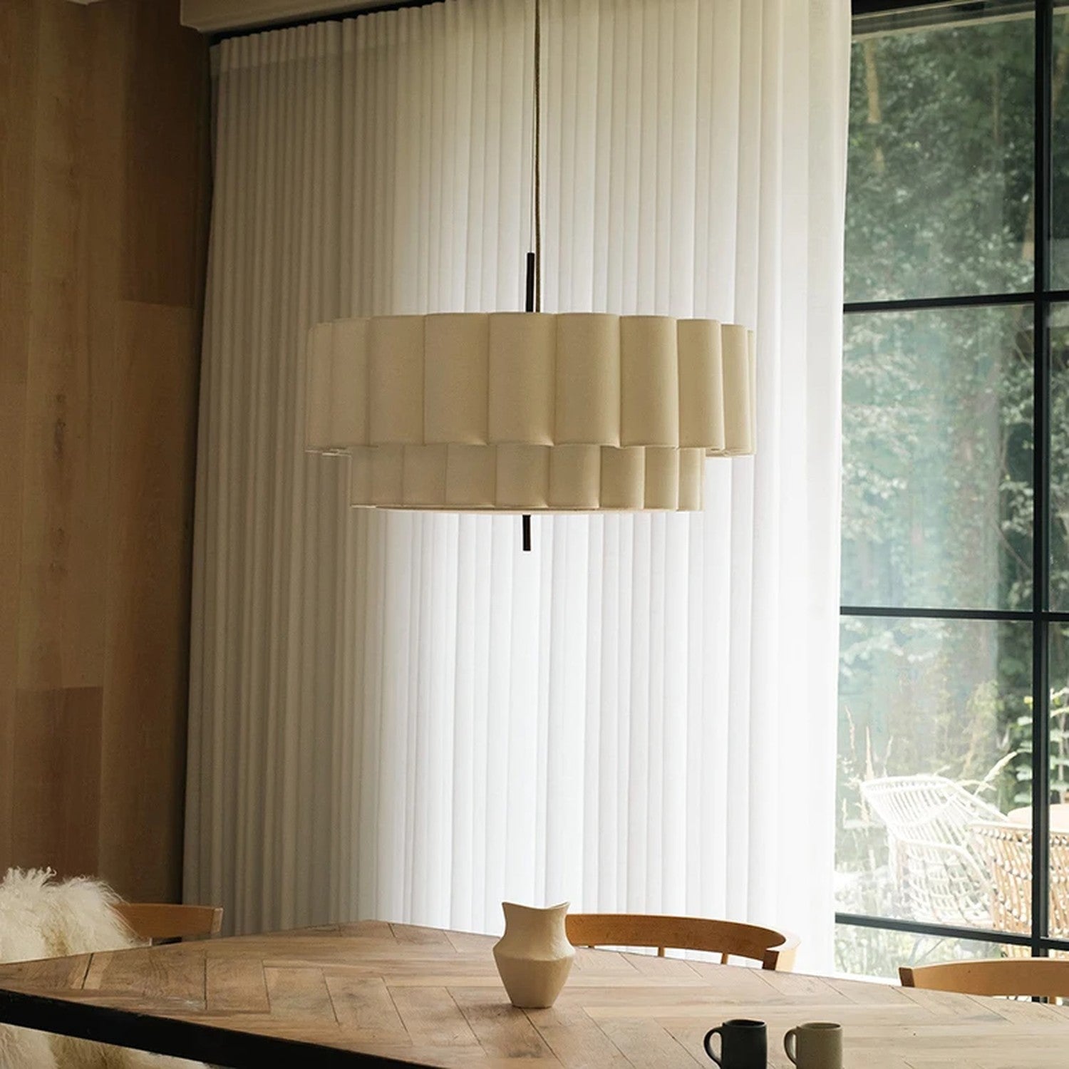 Suspension ronde en tissu beige éclairée au-dessus d'une table en bois près d'une grande fenêtre