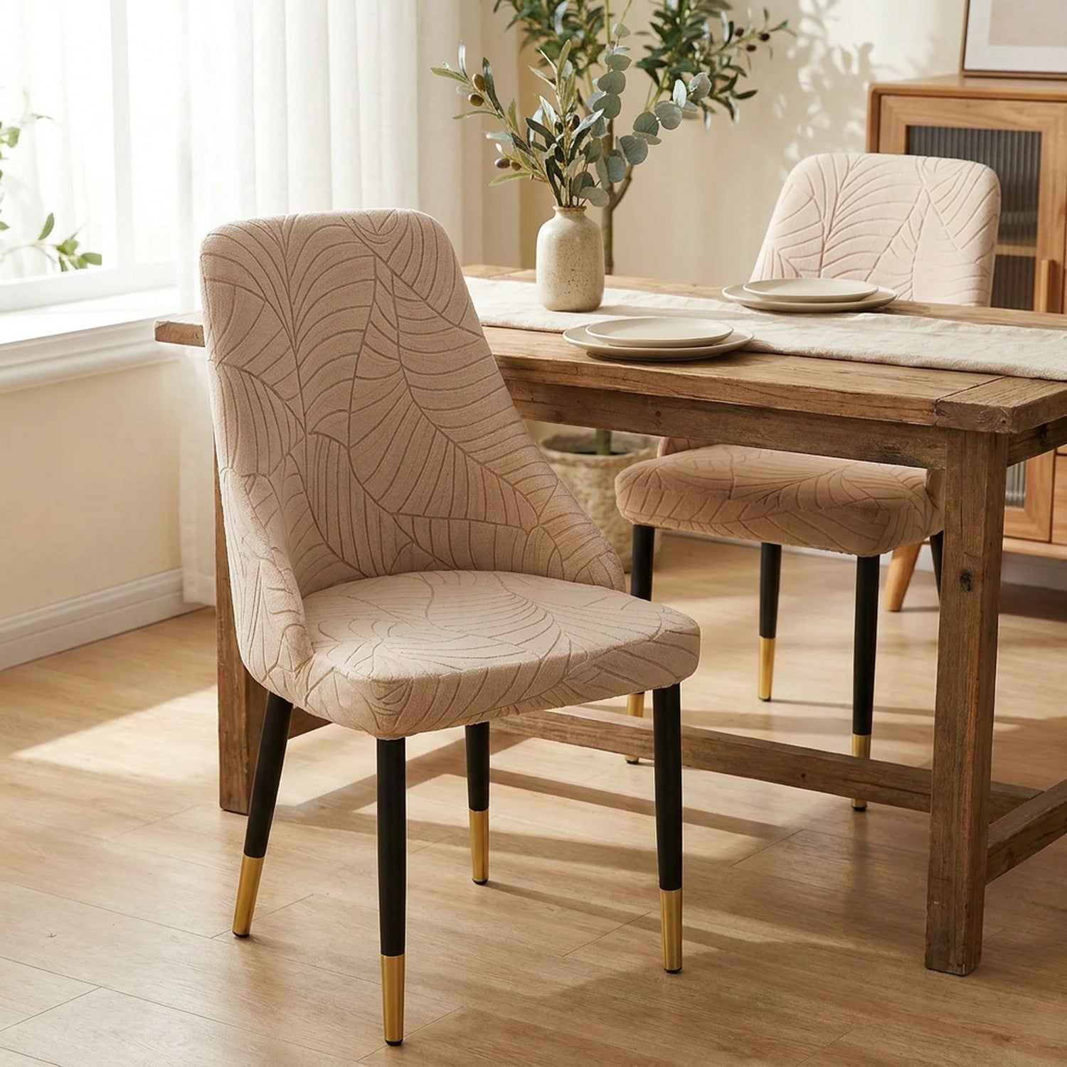 Deux chaises habillées de la housse beige au motif feuilles autour d'une table de salle à manger dressée