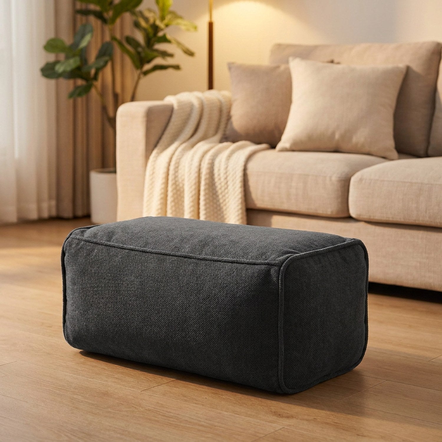 Pouf repose-pieds anthracite utilisé devant un canapé en lin dans un salon cosy