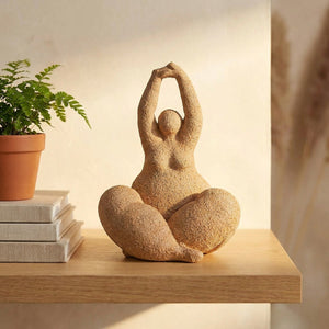Statue de femme ronde terracotta posée sur une étagère avec livres et plante verte
