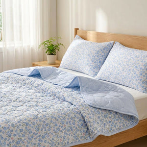 Couette d'été bleue à fleurs dépliée sur un lit avec ses taies assorties et son envers à carreaux