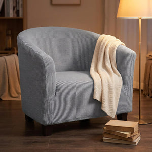 Housse de fauteuil cabriolet grise dans un coin lecture avec un plaid drapé et un lampadaire