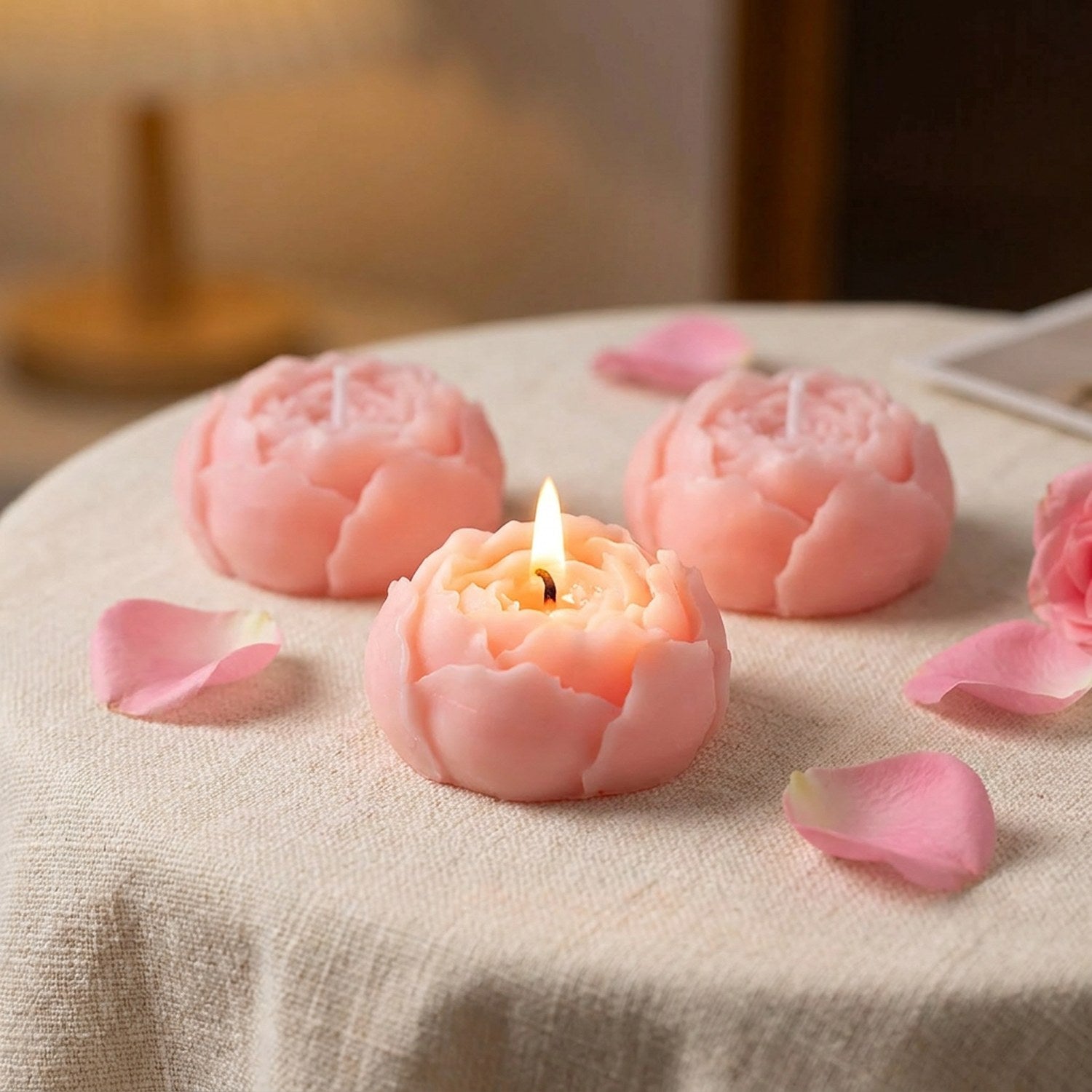 Bougies parfumées en forme de rose dont une allumée sur une nappe en lin avec pétales