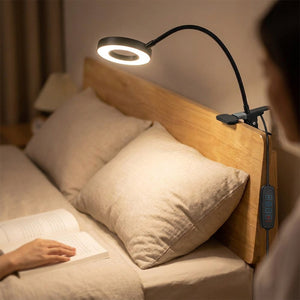 Lampe pince clipsée sur une tête de lit en bois éclairant une lecture du soir