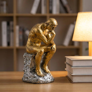 Statue Le Penseur de Rodin dorée sur un bureau avec des livres et une lampe chaleureuse