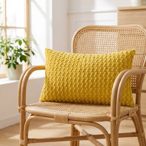 housse de coussin en maille texturée jaune moutarde sur un fauteuil en rotin près d'une fenêtre