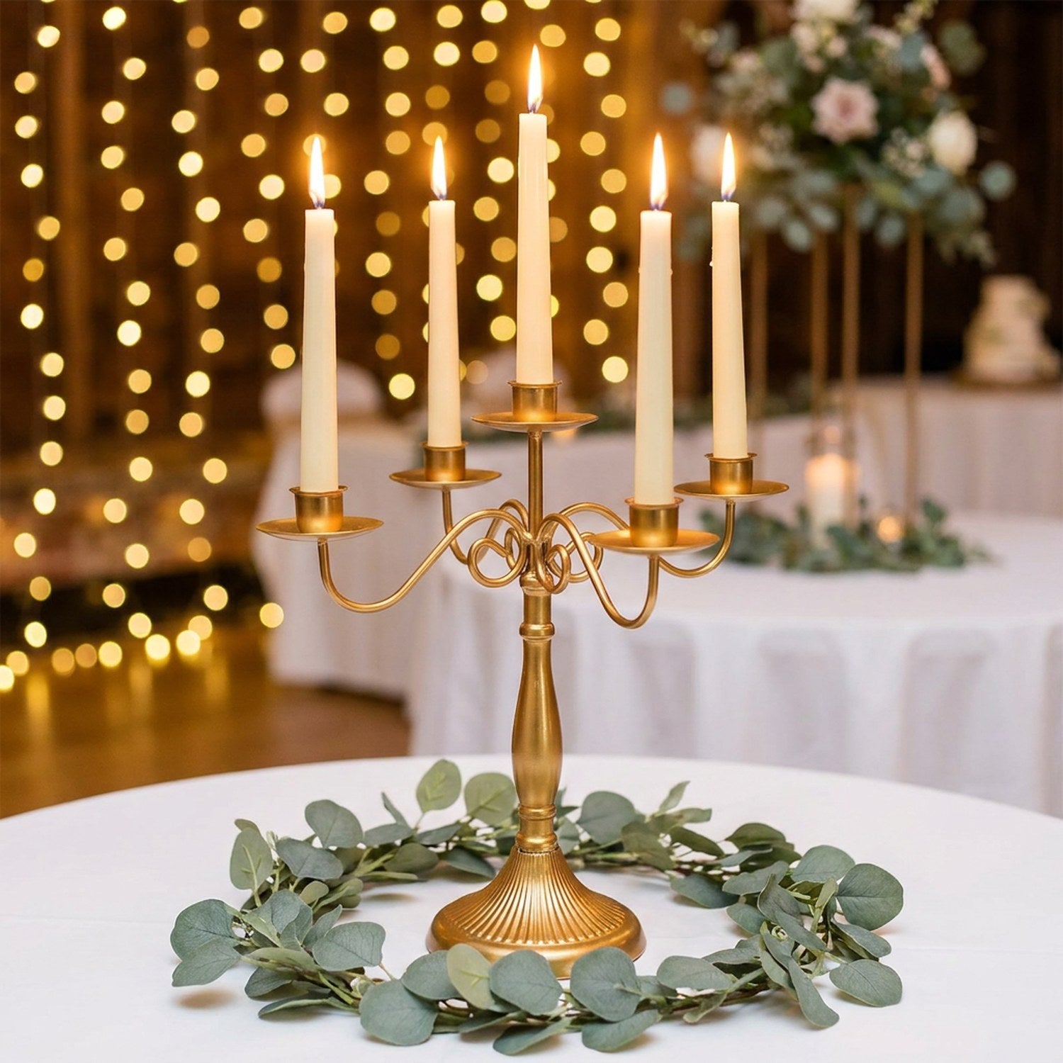 Chandelier doré à cinq branches en centre de table de mariage avec guirlande d'eucalyptus