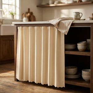 Rideau beige installé sous un îlot de cuisine dévoilant de la vaisselle rangée