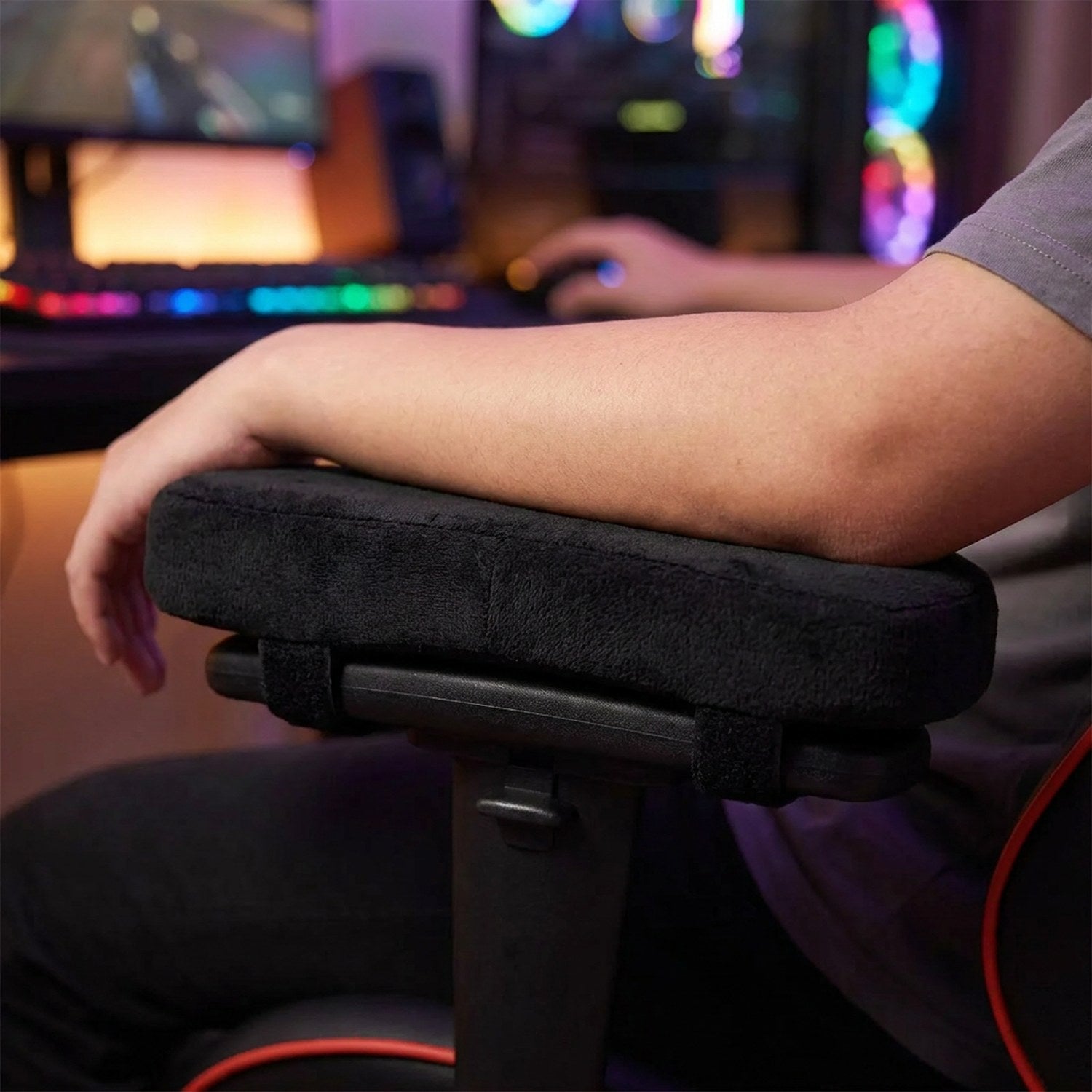 Avant-bras posé sur le coussinet d'accoudoir noir devant un setup gaming