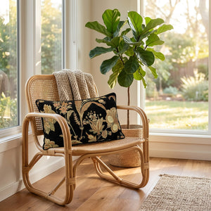 Coussin lombaire a motif floral pose sur un fauteuil en rotin pres d'une fenetre