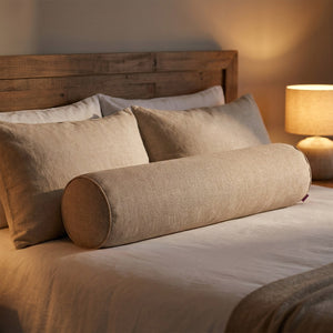 Housse de traversin cylindrique beige posée sur un lit devant les oreillers avec une lampe de chevet allumée