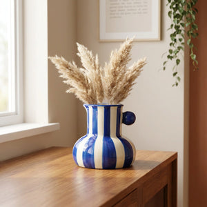 Vase rayé bleu avec herbes de la pampa sur une console en bois dans un salon lumineux