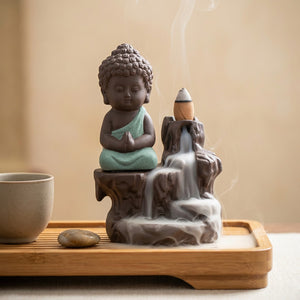 Brûleur d'encens bouddha posé sur un plateau en bambou avec une tasse de thé et un galet