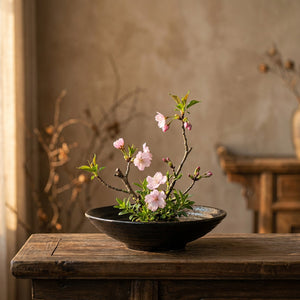Composition florale ikebana dans un vase en céramique noire sur une table en bois