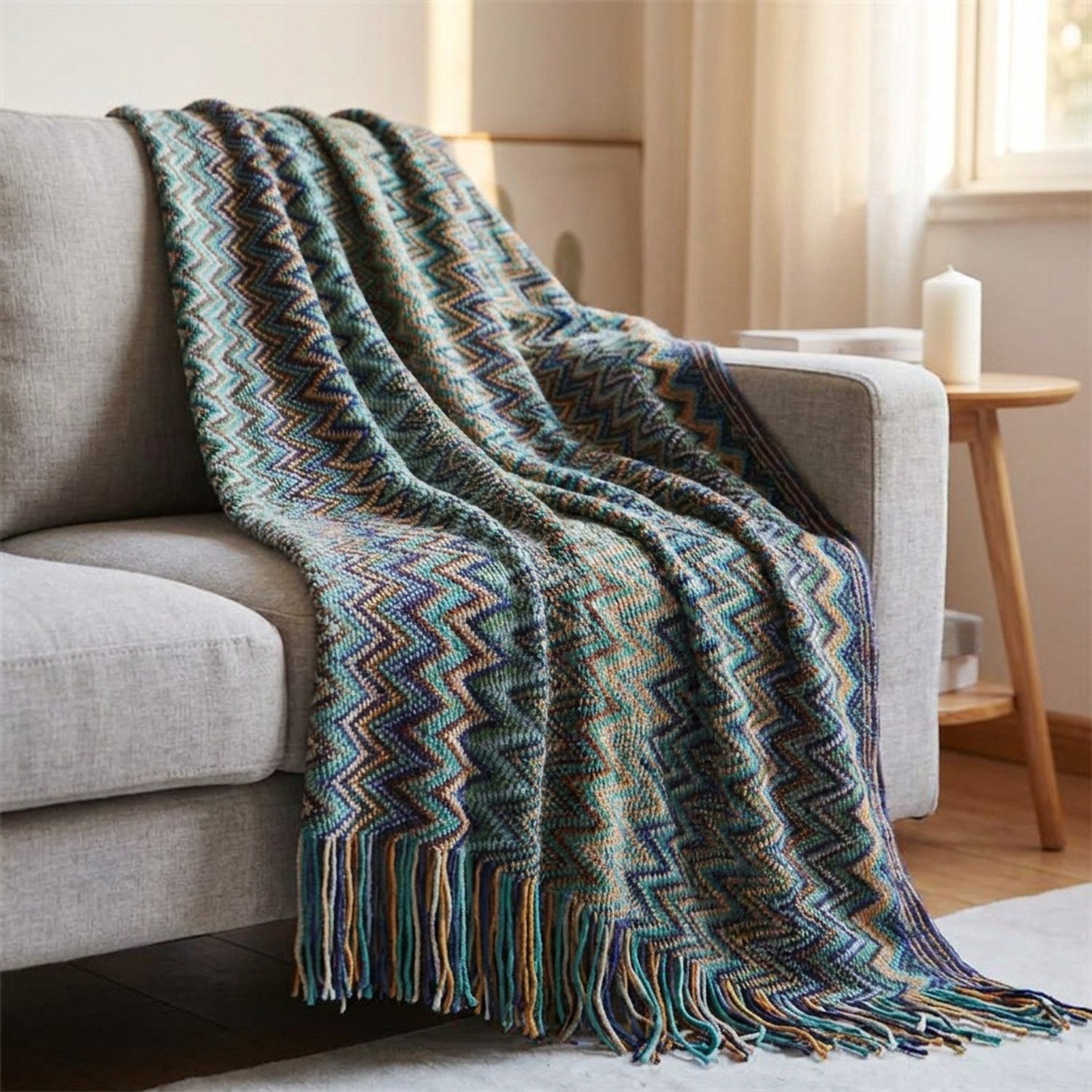Plaid tricoté drapé sur un canapé en lin gris avec bougie sur guéridon