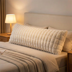 Traversin en peluche blanche sur un lit avec lampe de chevet allumée