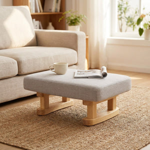 Tabouret rembourré gris utilisé comme table basse d'appoint dans un salon