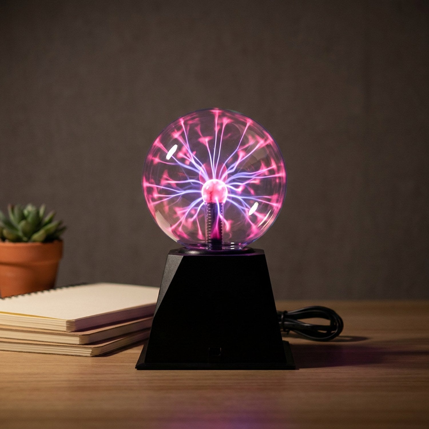 Lampe boule de plasma allumée sur un bureau avec cahiers et plante succulente