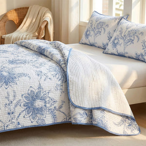 Couvre-lit fleuri bleu et blanc replié au pied du lit dans une chambre lumineuse