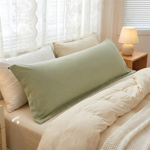 Taie de traversin longue verte habillant un long coussin sur un lit avec lampe de chevet